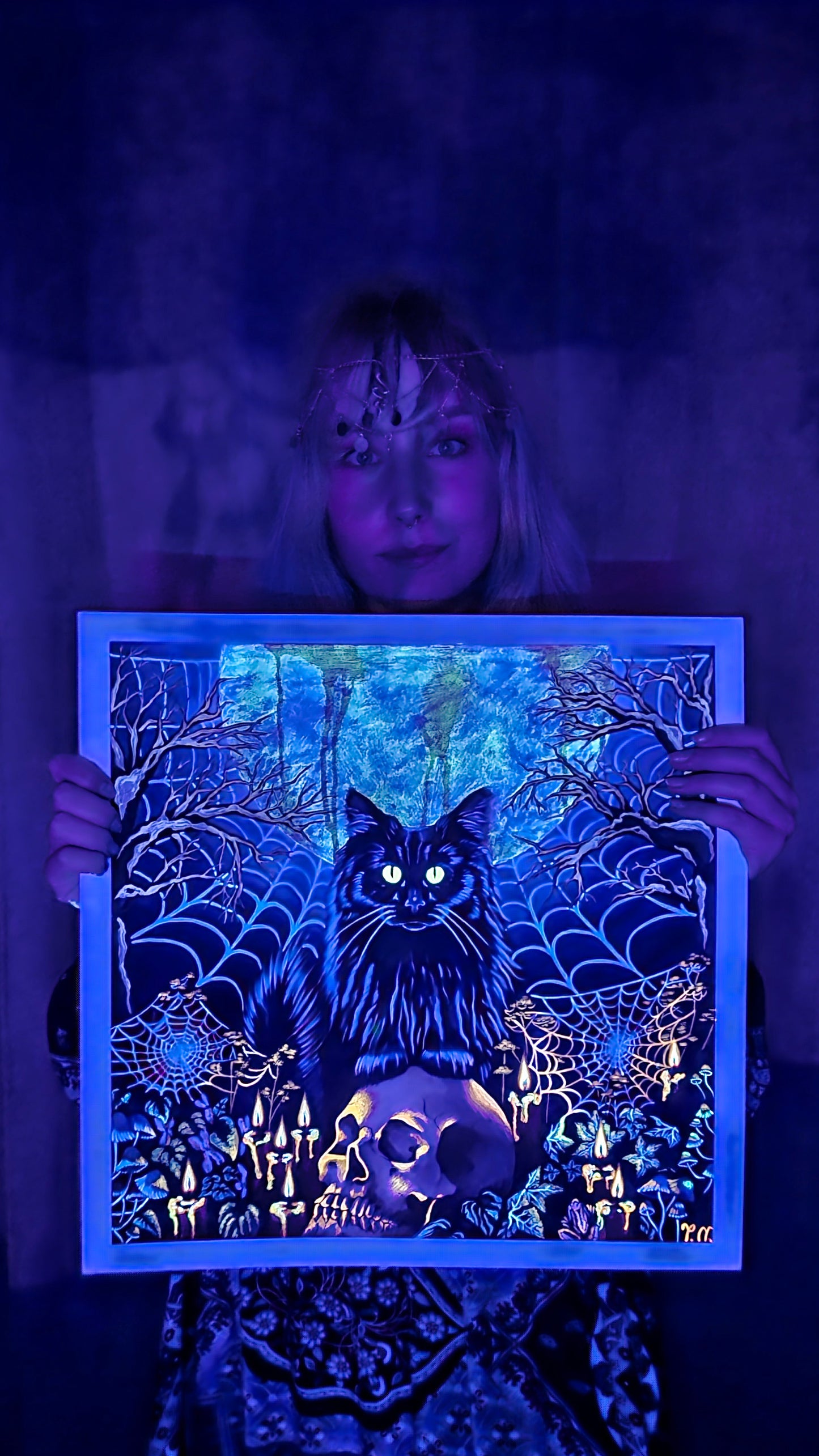 Person holding a glowing black cat artwork in a dark setting