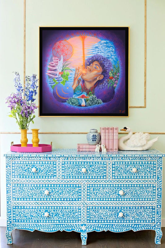 A framed artwork featuring a psychedelic design with a figure and abstract patterns, displayed on a blue-patterned furniture in a home setting.
