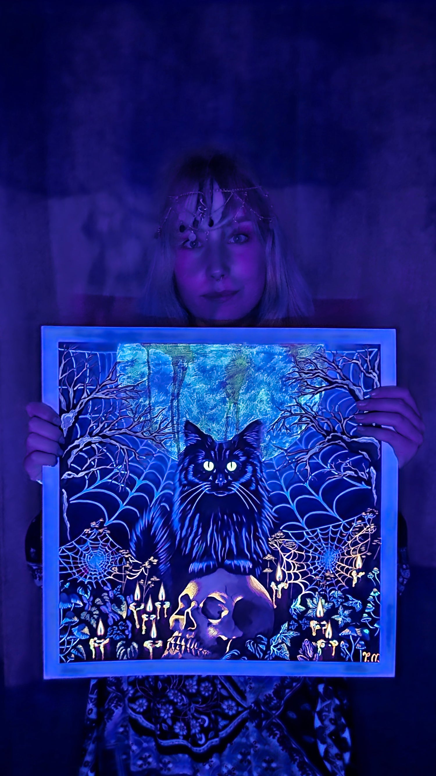 Person holding a glowing black cat artwork in a dark setting
